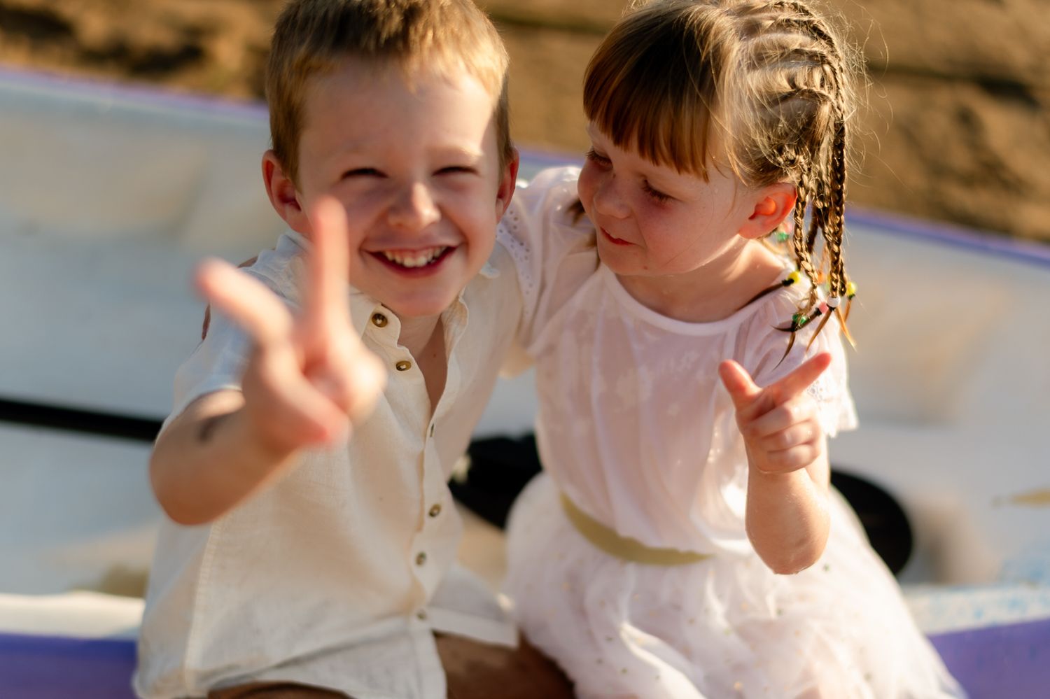 Two happy children flash peace signs while sitting together in warm sunlight.