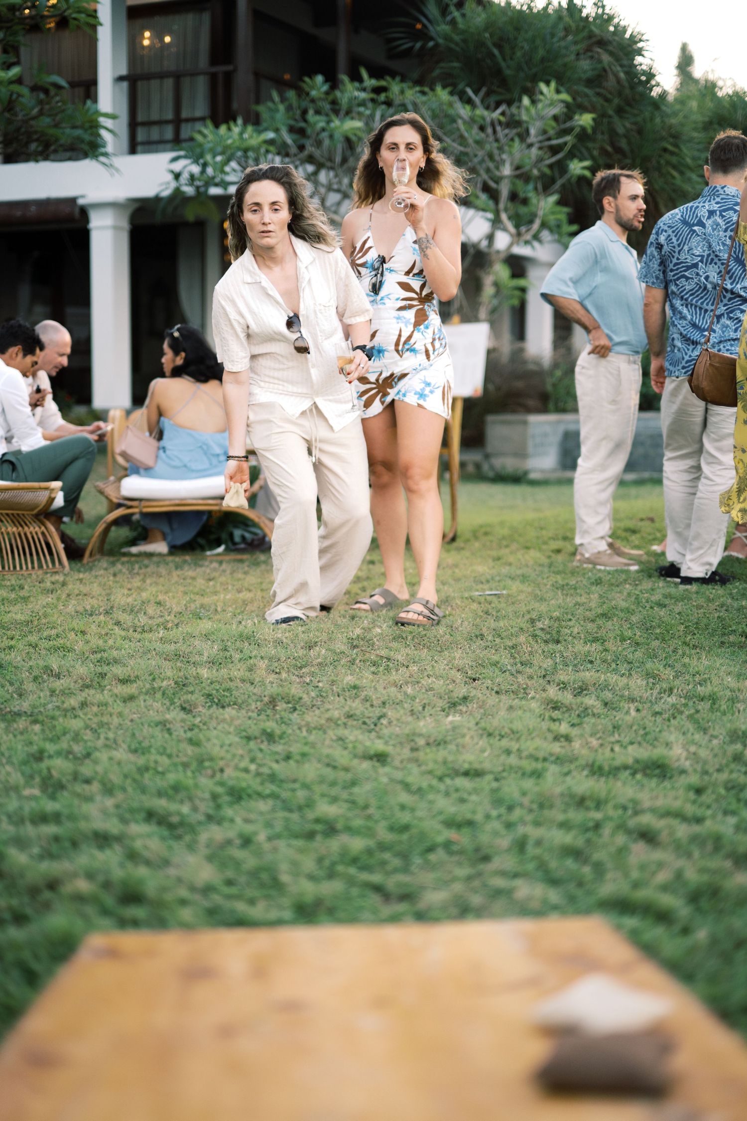 Wedding guests play cornhole lawn game on green grass during outdoor garden reception.