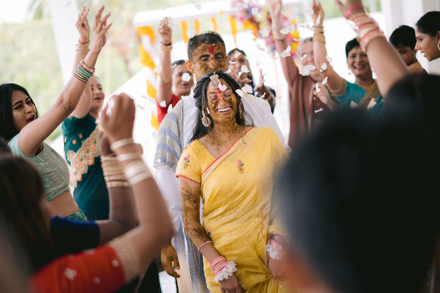 Guests celebrate at a vibrant Indian wedding ceremony with colorful attire and joyful raised hands.