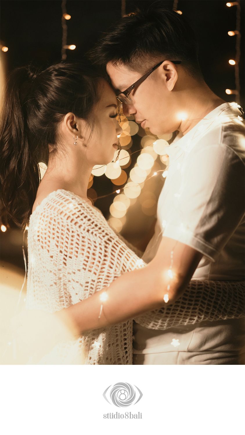 Romantic couple embracing with glowing fairy lights, sharing an intimate moment in a warm bokeh-lit setting.