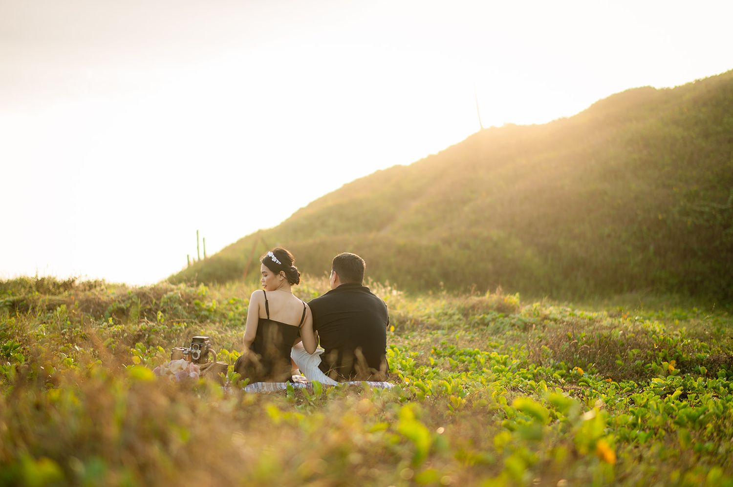 Couple sitting together on a grassy hillside at golden sunset during outdoor wedding shoot.