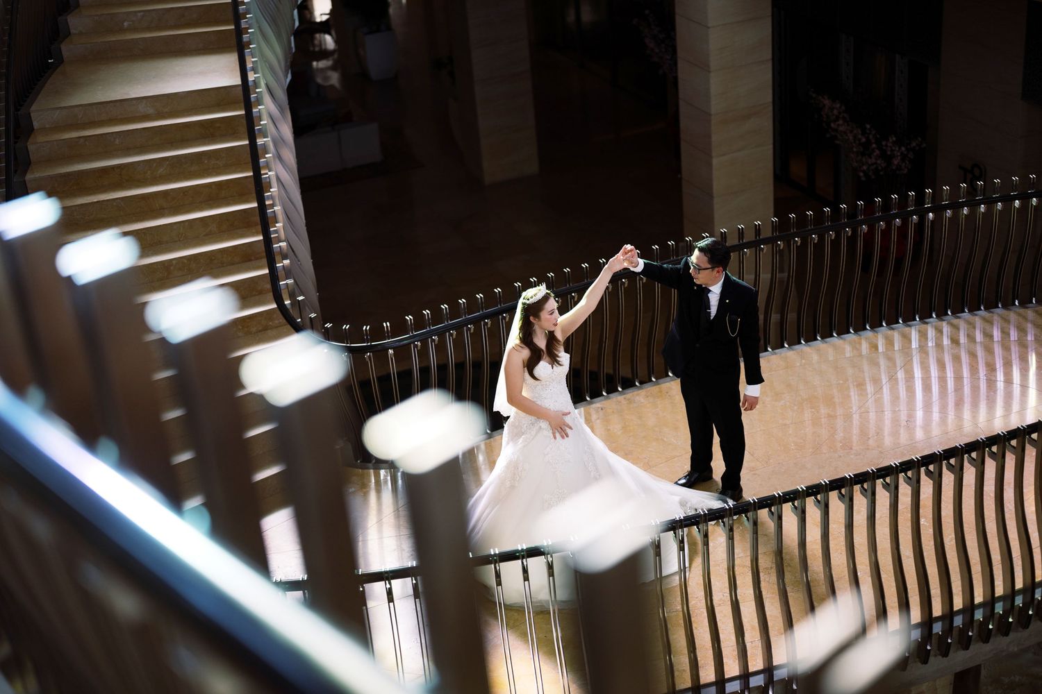 Bride and groom dancing on a grand staircase balcony in an elegant wedding venue.