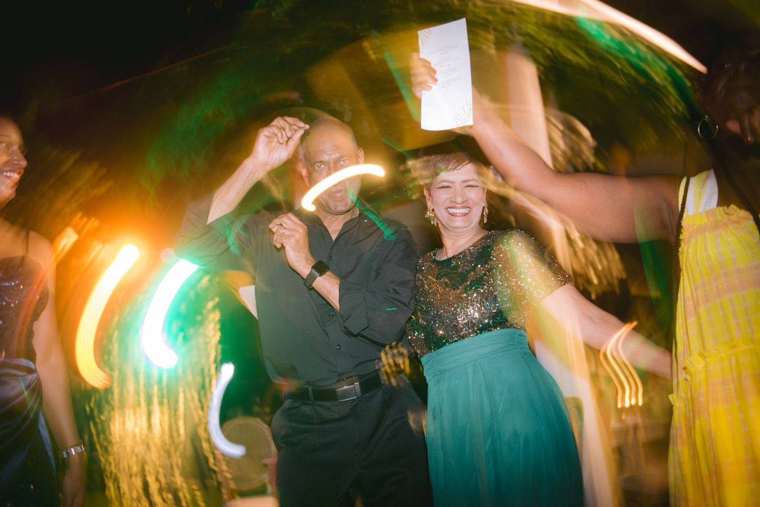 Joyful couple dancing at a festive night party with colorful light streaks and glowing accessories.