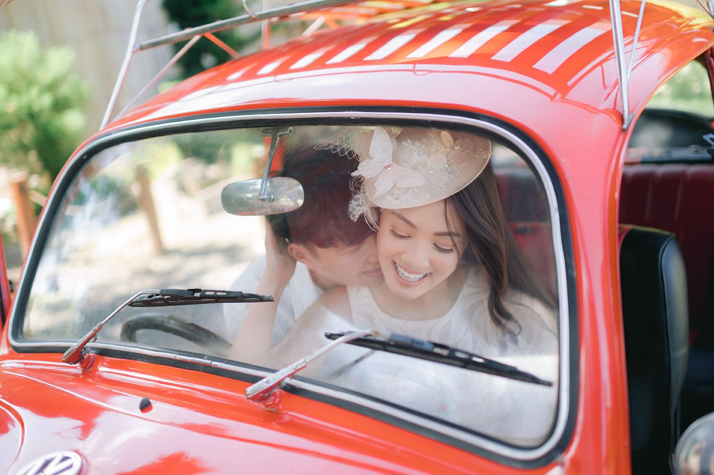 Couple sharing a romantic kiss inside a vintage red Volkswagen Beetle car on their wedding day.