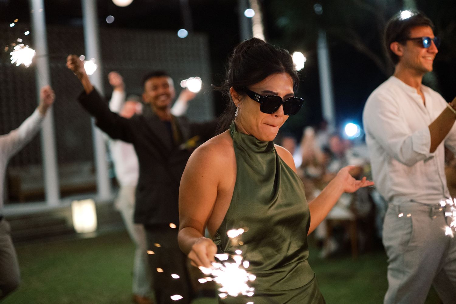 Woman in green dress holding sparklers at outdoor wedding reception at night.