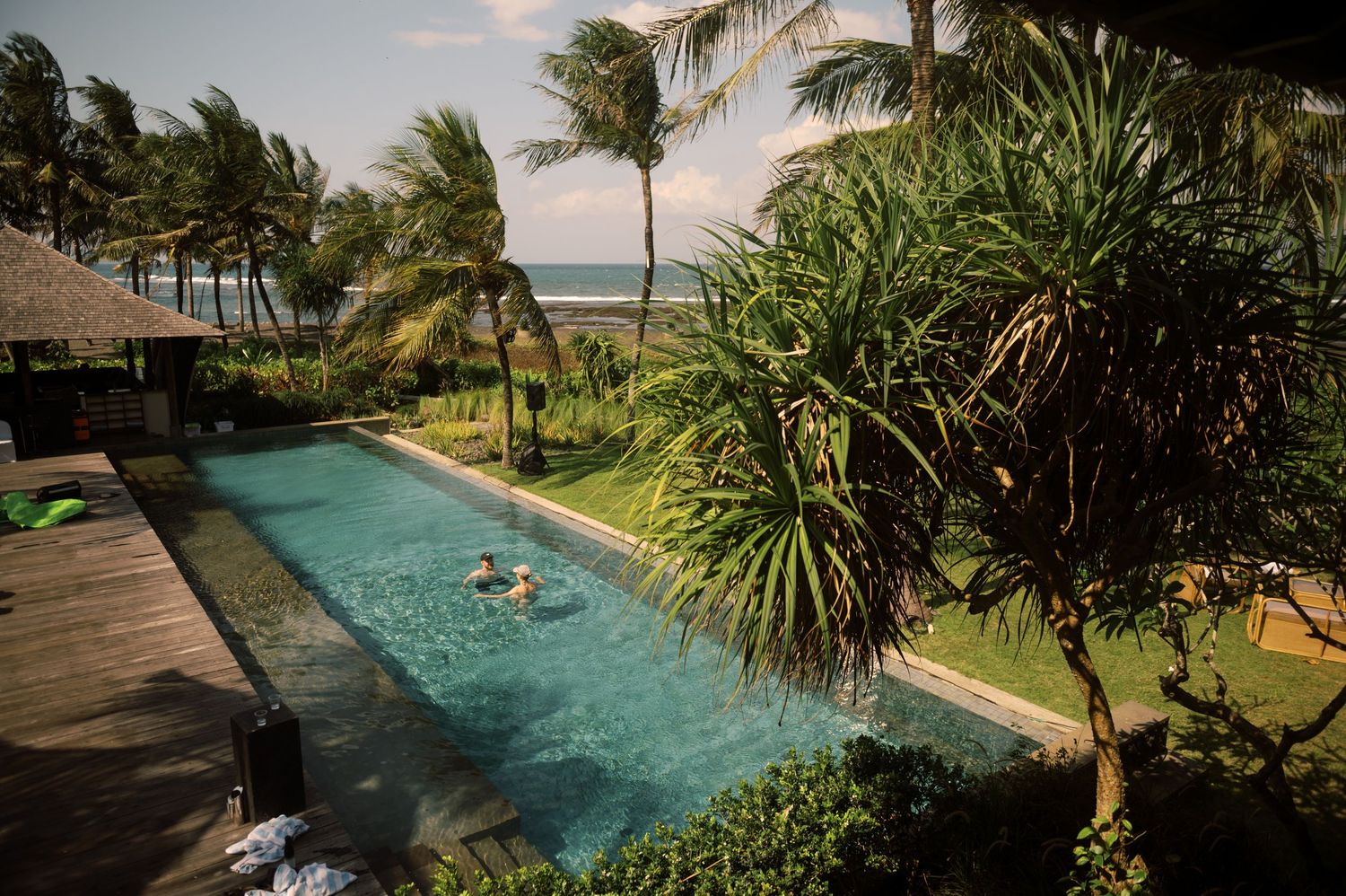 Tropical infinity pool with palm trees and ocean view, person swimming in turquoise water at a luxury resort.
