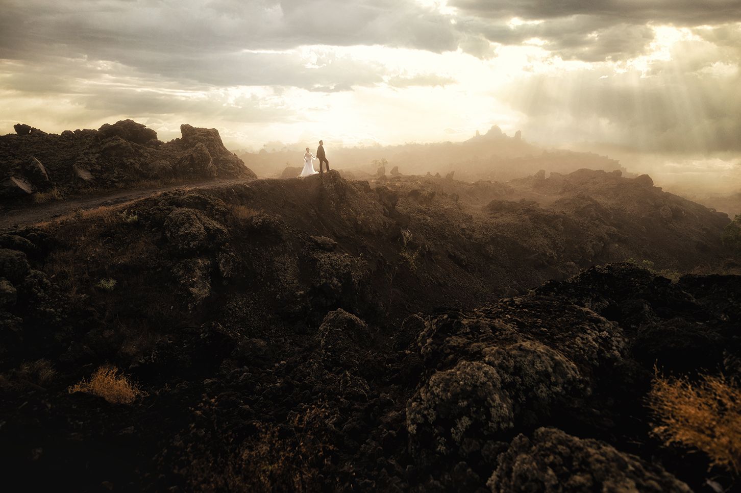 A lone figure stands on a dramatic volcanic landscape bathed in golden sunlight breaking through stormy clouds.
