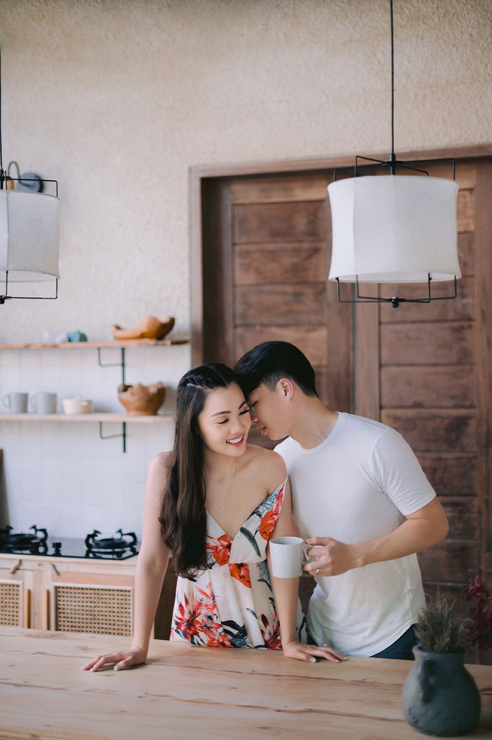 Romantic couple sharing an intimate moment in a modern kitchen, man kissing woman's cheek while holding a coffee mug.