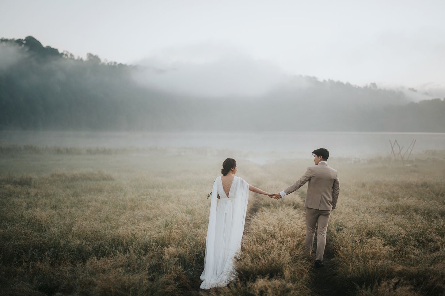 Bride and groom holding hands in misty mountain meadow, romantic outdoor wedding photography.