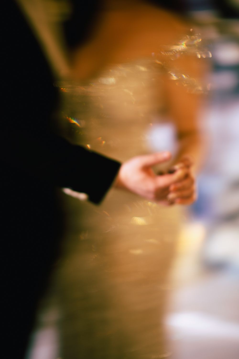 Blurred romantic photo of couple holding hands at a wedding reception with warm golden bokeh lighting.