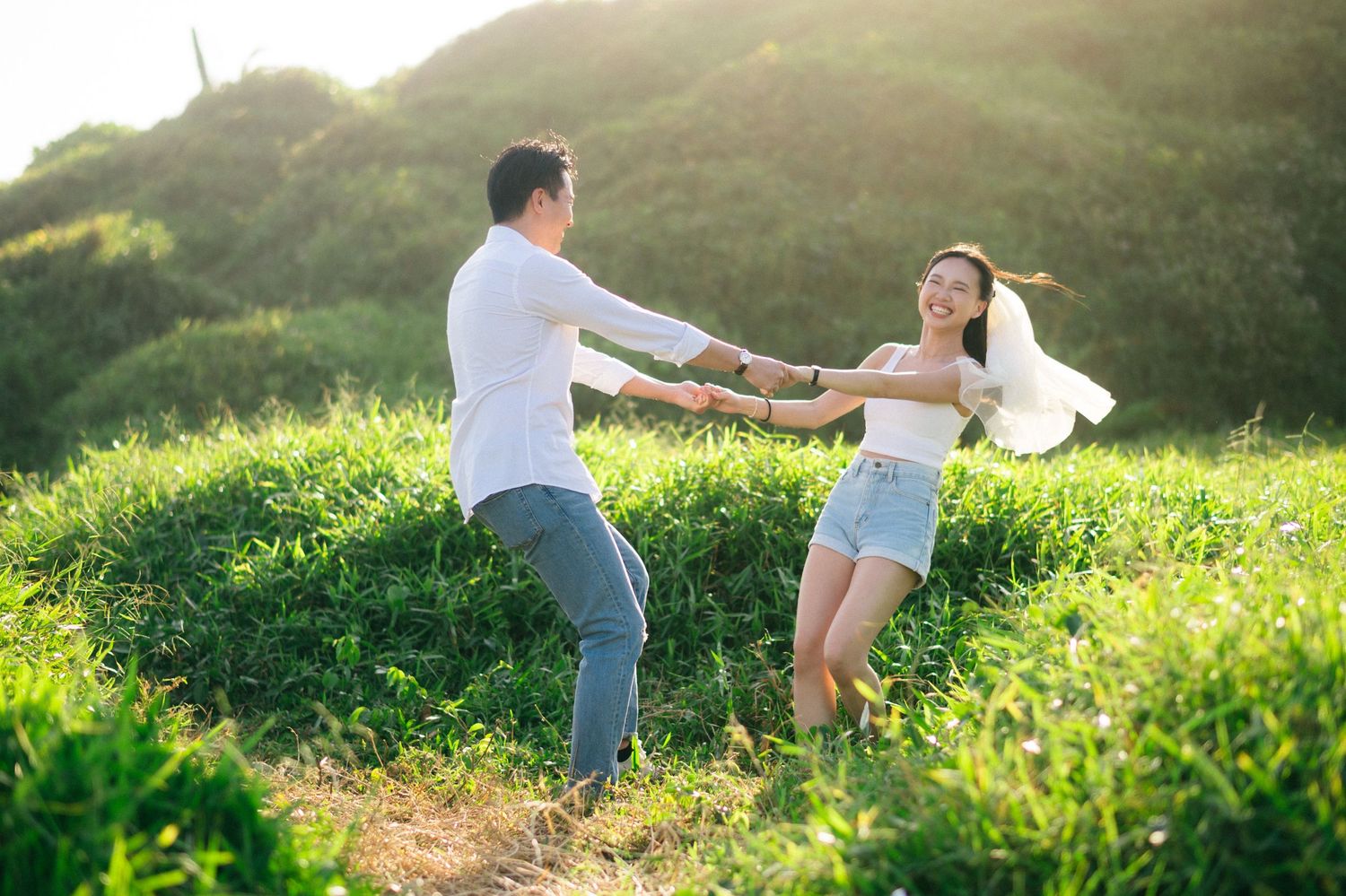 Happy couple holding hands and spinning together in a lush green field.