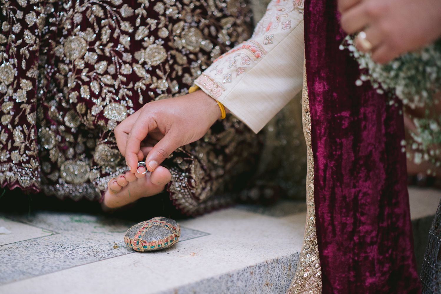 Close-up of hands in traditional South Asian bridal attire adjusting ornate wedding sandals on marble steps.