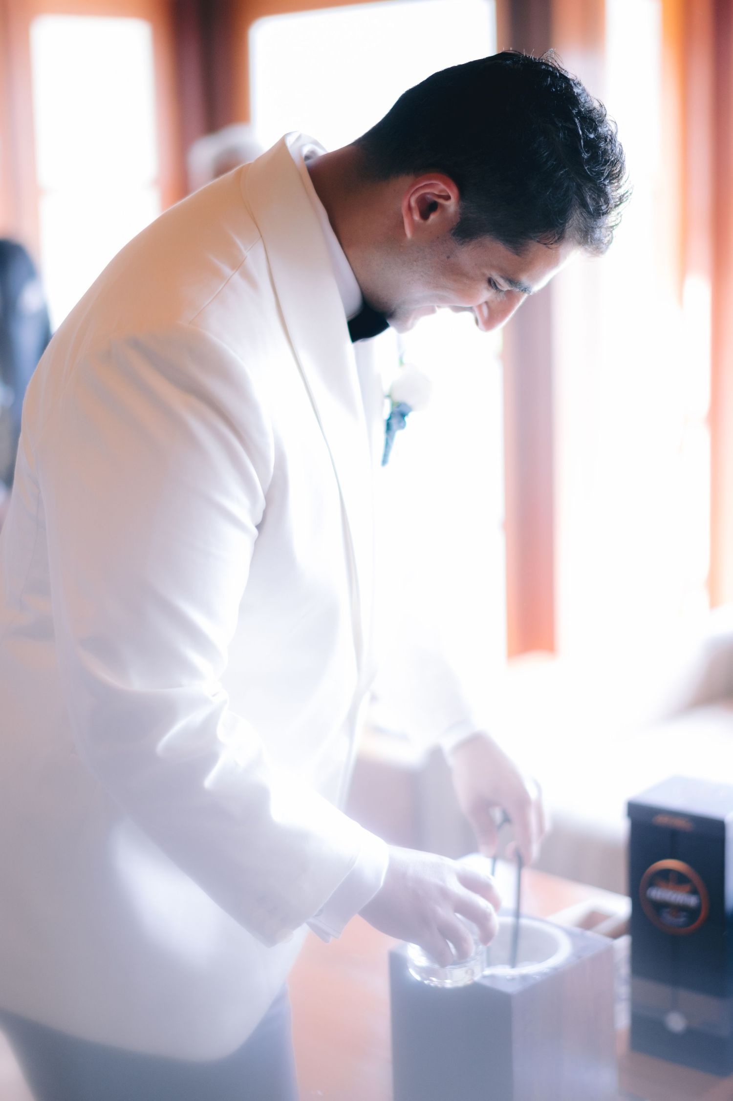 Groom in white tuxedo jacket carefully prepares wedding rings at a table before the ceremony.