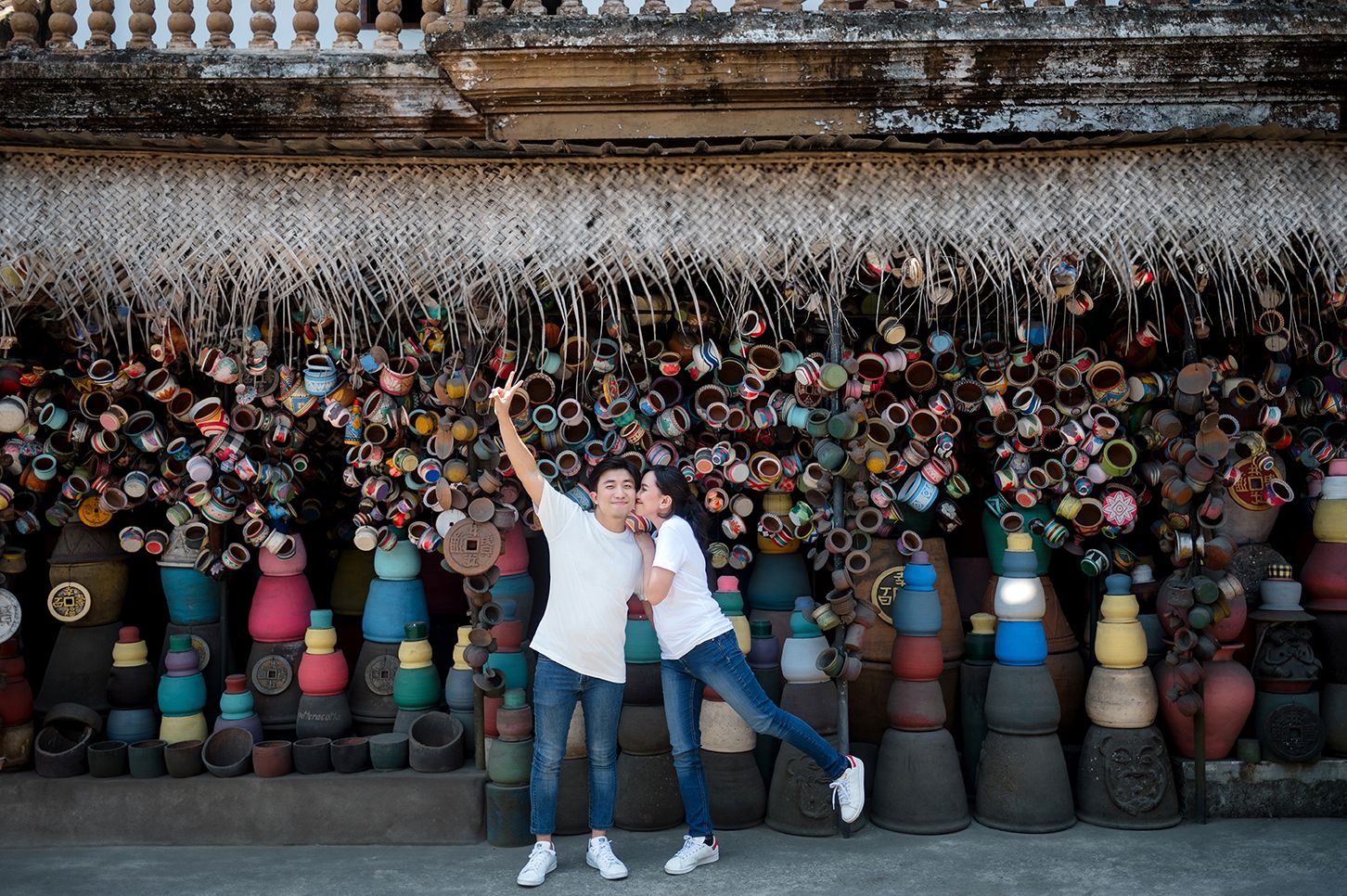 Couple posing joyfully in front of colorful hanging decorations and ceramic pots at a temple.