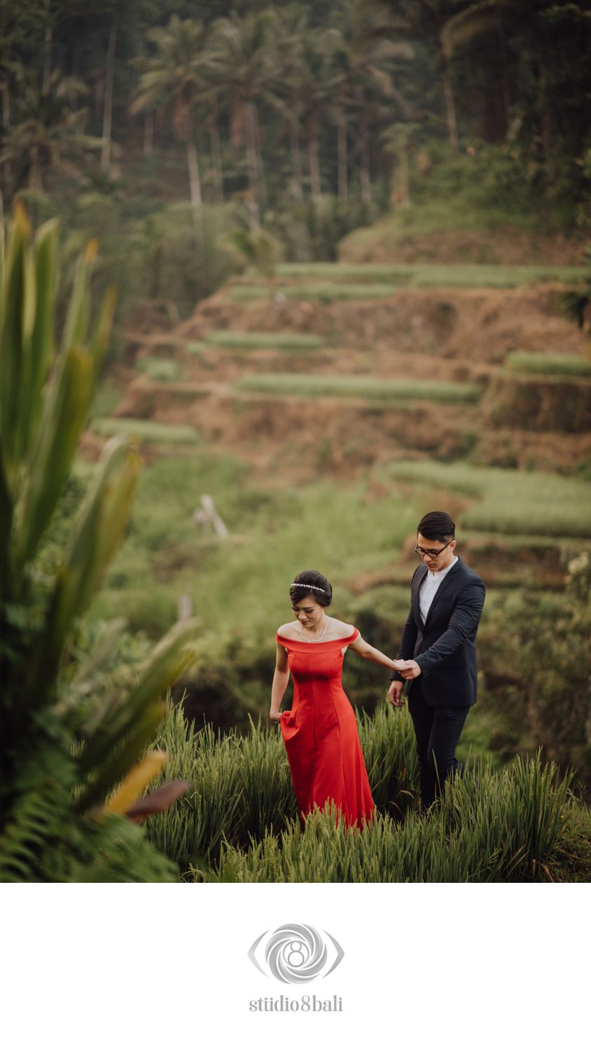 Couple in red dress and suit posing in lush Bali rice terraces for a romantic pre-wedding photoshoot.