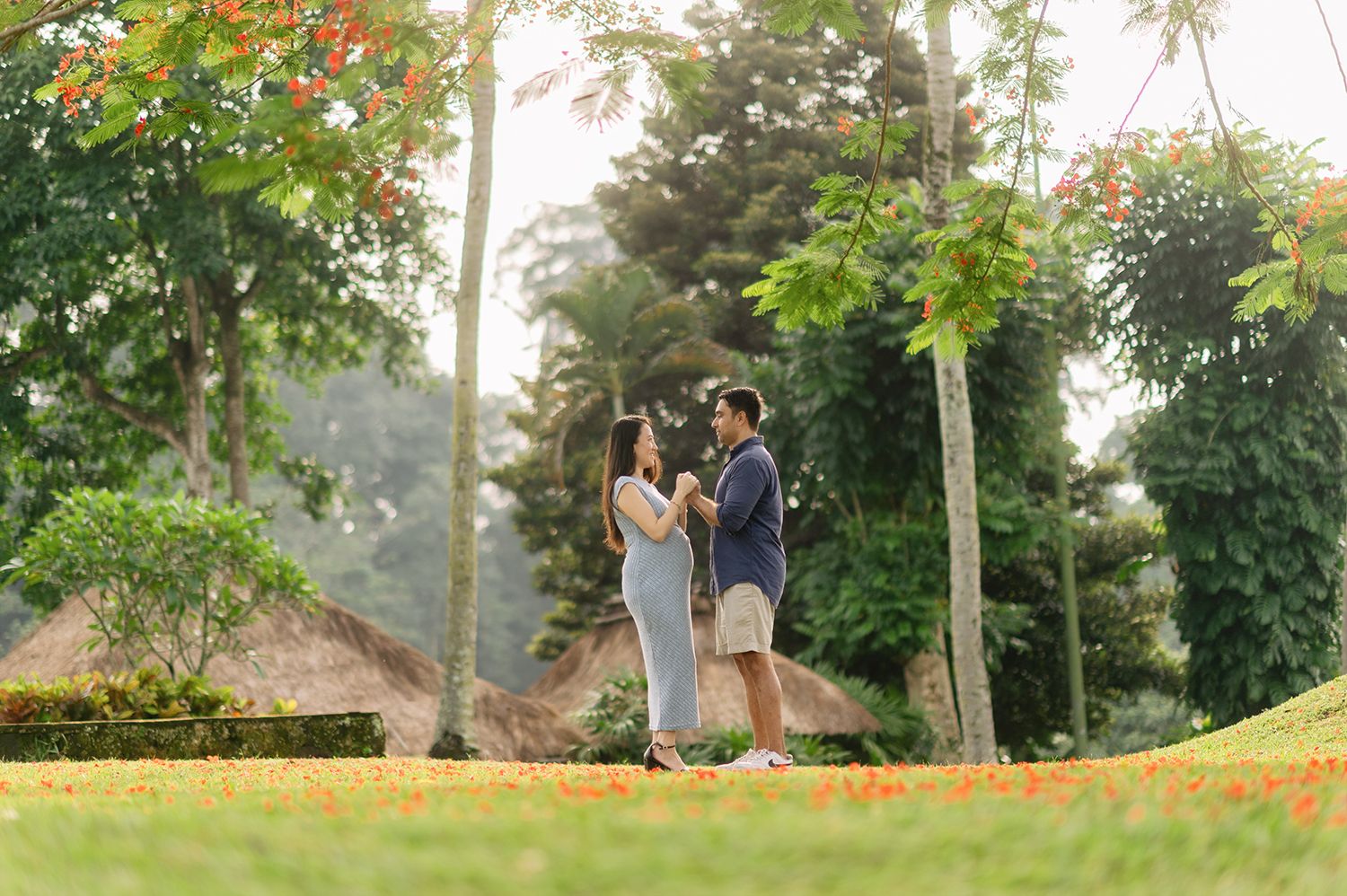 Couple standing together in a lush tropical garden with orange flowers and tall trees in warm sunlight Maya Ubud Resort and Spa in Bali.
