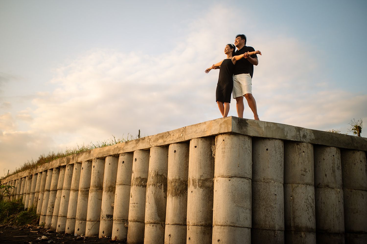 Couple standing together on top of a concrete wall structure at sunset.