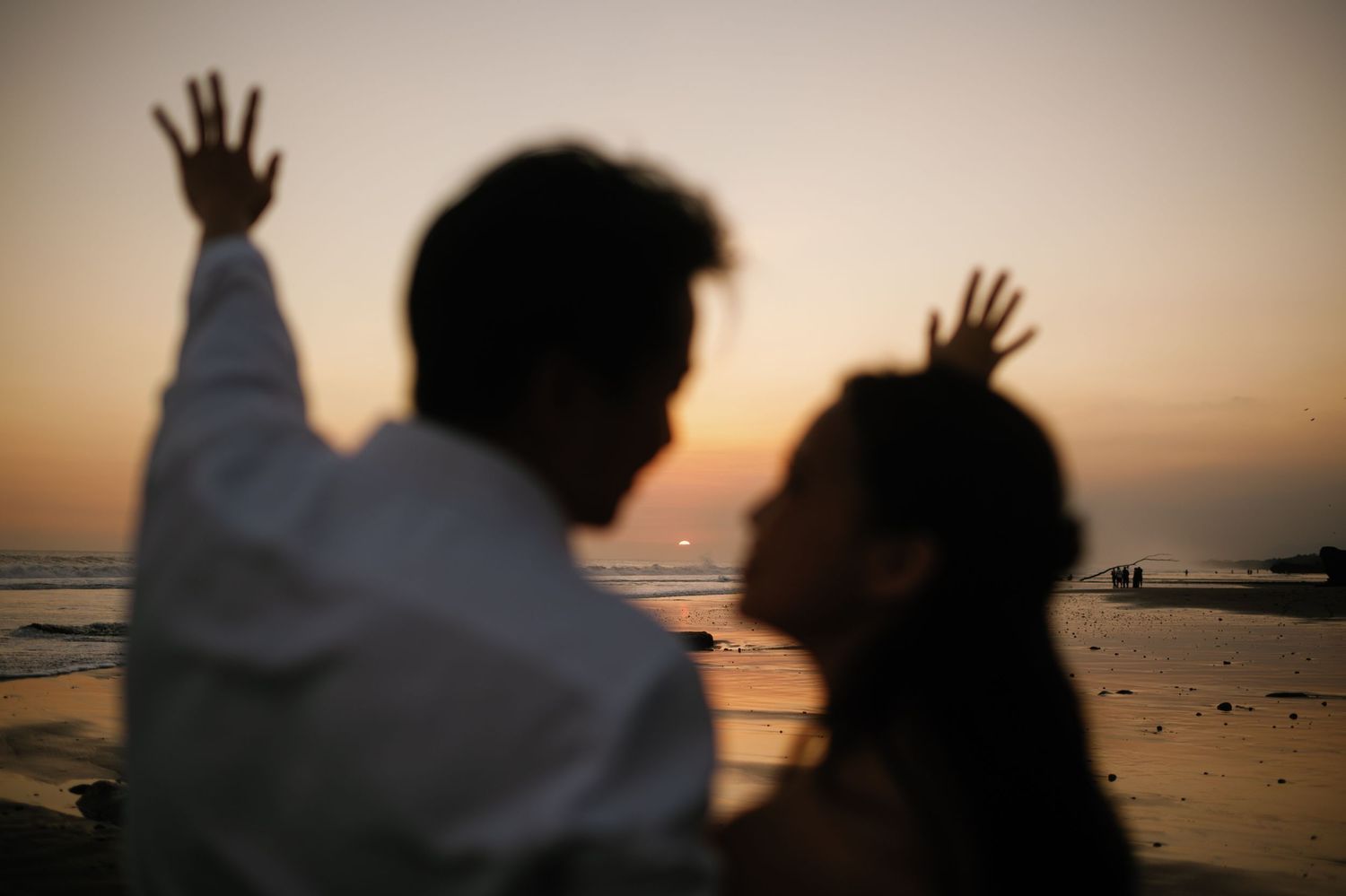 Silhouette of a couple raising hands at a romantic beach sunset.