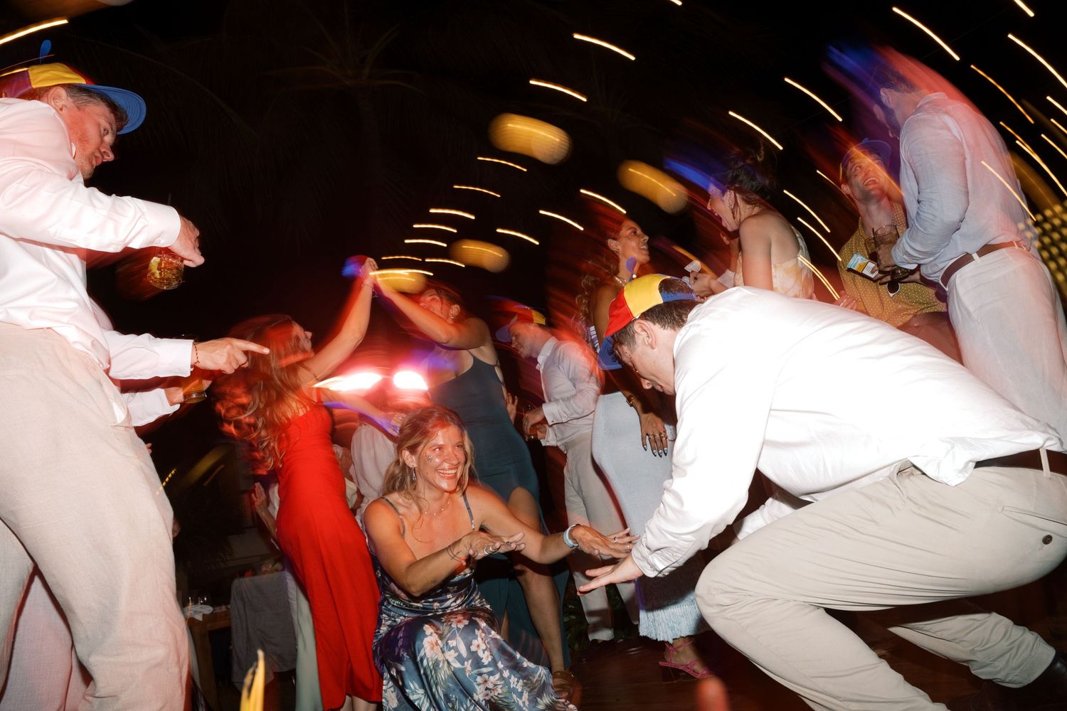 Guests dancing energetically at a lively wedding reception party with colorful lights and motion blur.