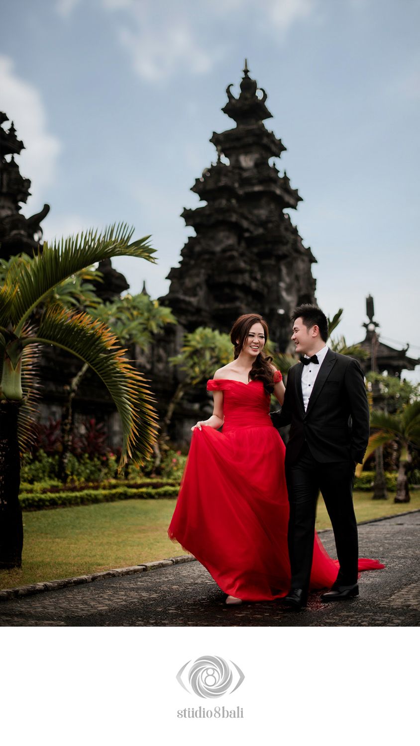 Couple in red ball gown and tuxedo sharing a romantic moment at a Balinese temple garden.