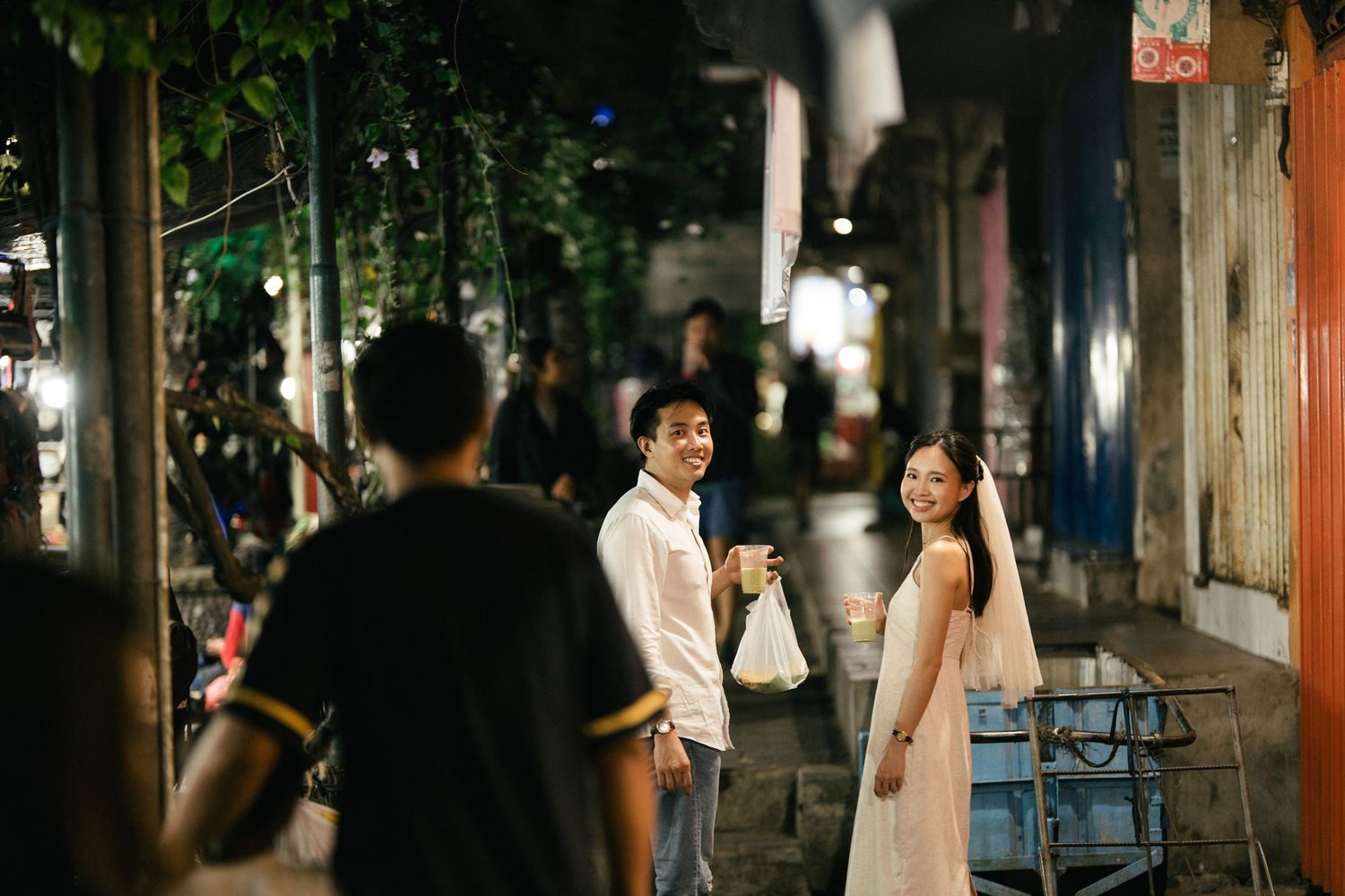 Smiling couple in white outfits on a lively night market street.