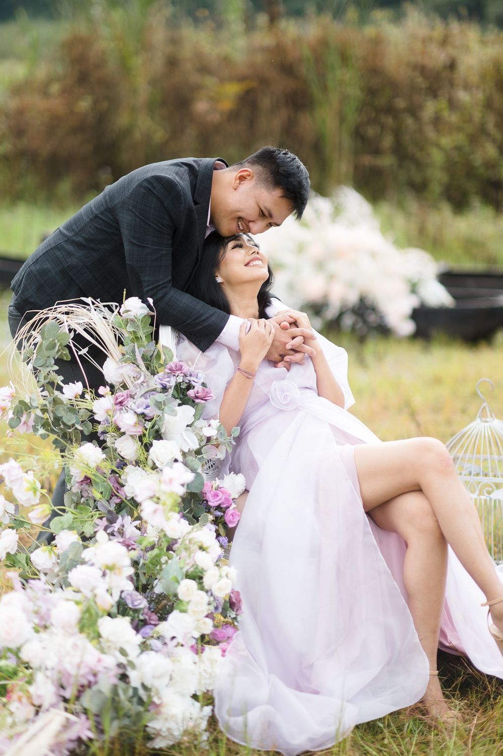 A couple shares a romantic moment surrounded by white and purple flowers in an outdoor garden setting.