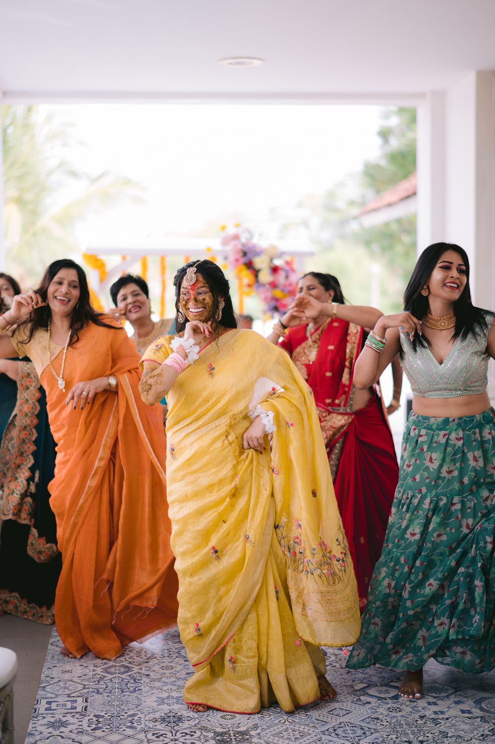 Women in colorful sarees and lehengas dancing joyfully at a vibrant Indian wedding celebration.