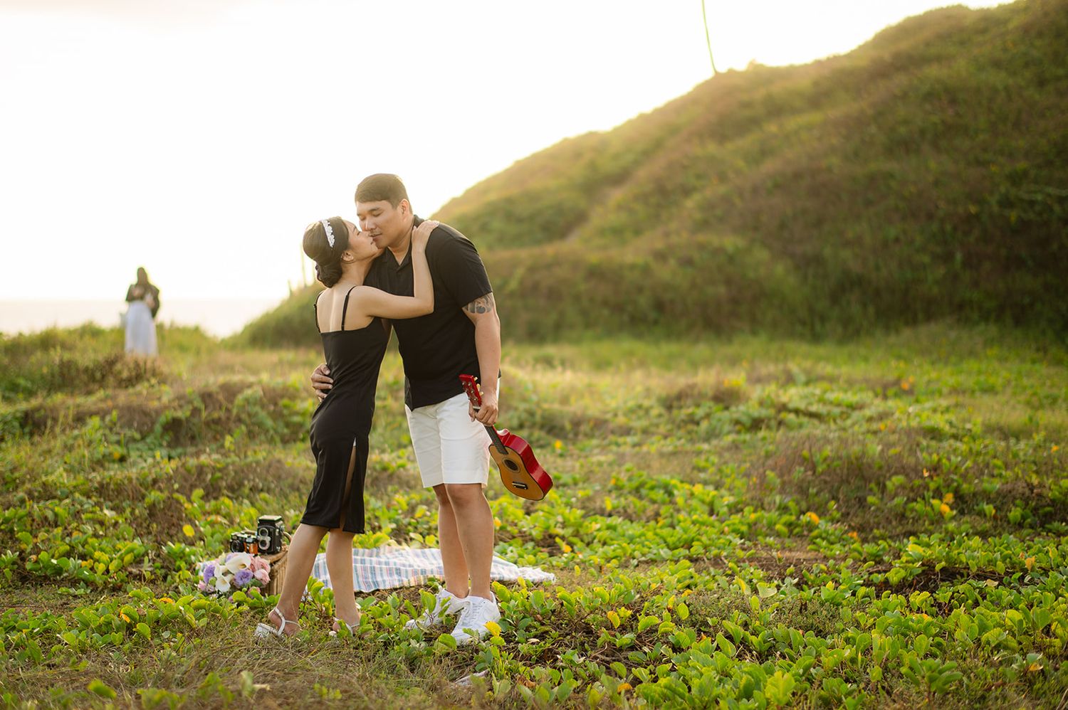 Couple sharing romantic kiss on green coastal meadow during golden hour sunset near the beach.