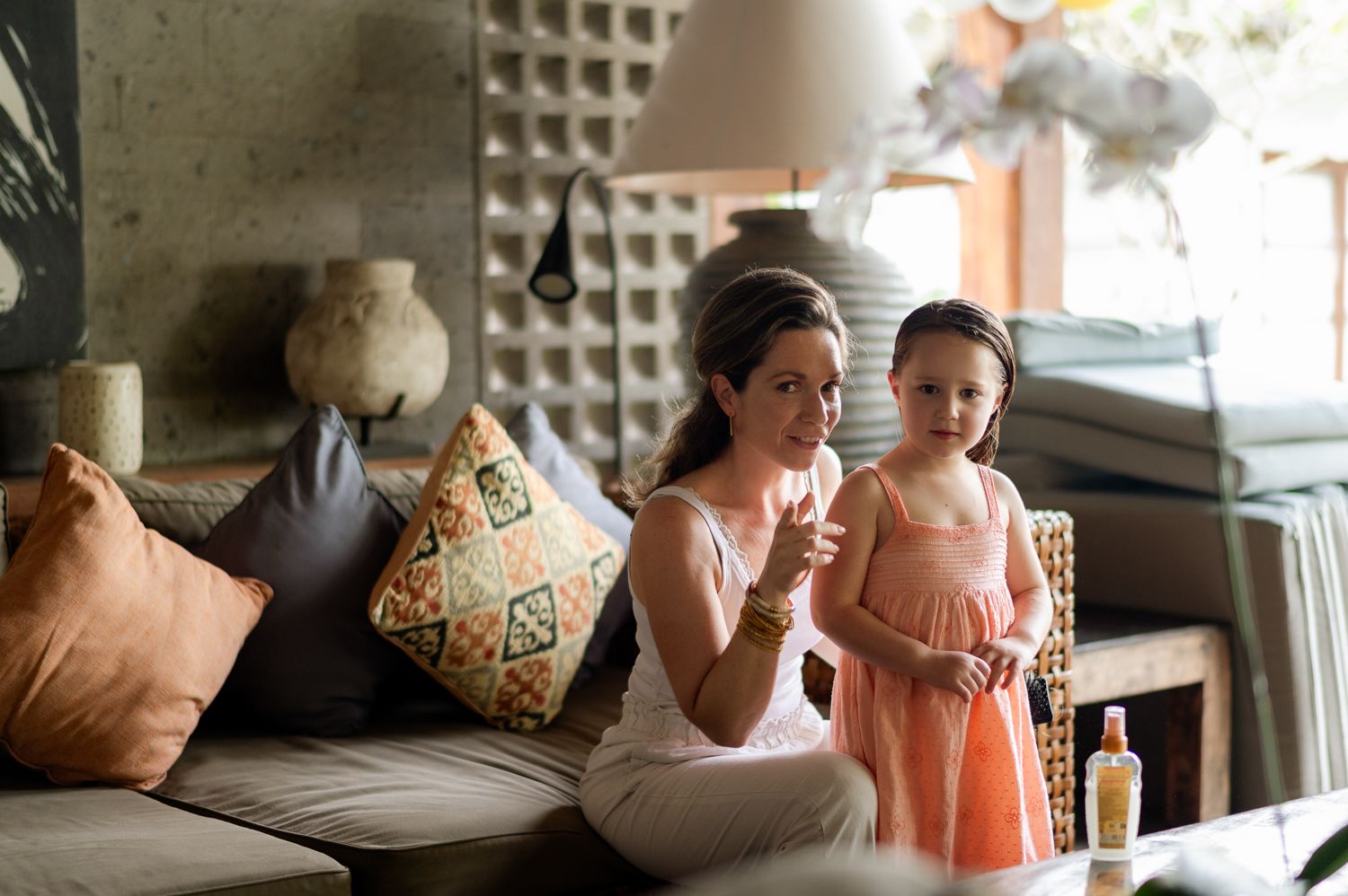 A mother and young daughter sit together on a couch blowing bubbles in a cozy living room.