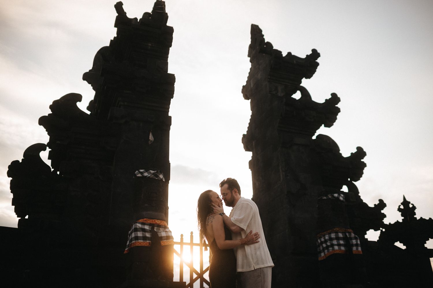Couple embracing at sunset in front of ornate Balinese temple gates in Bali, Indonesia.