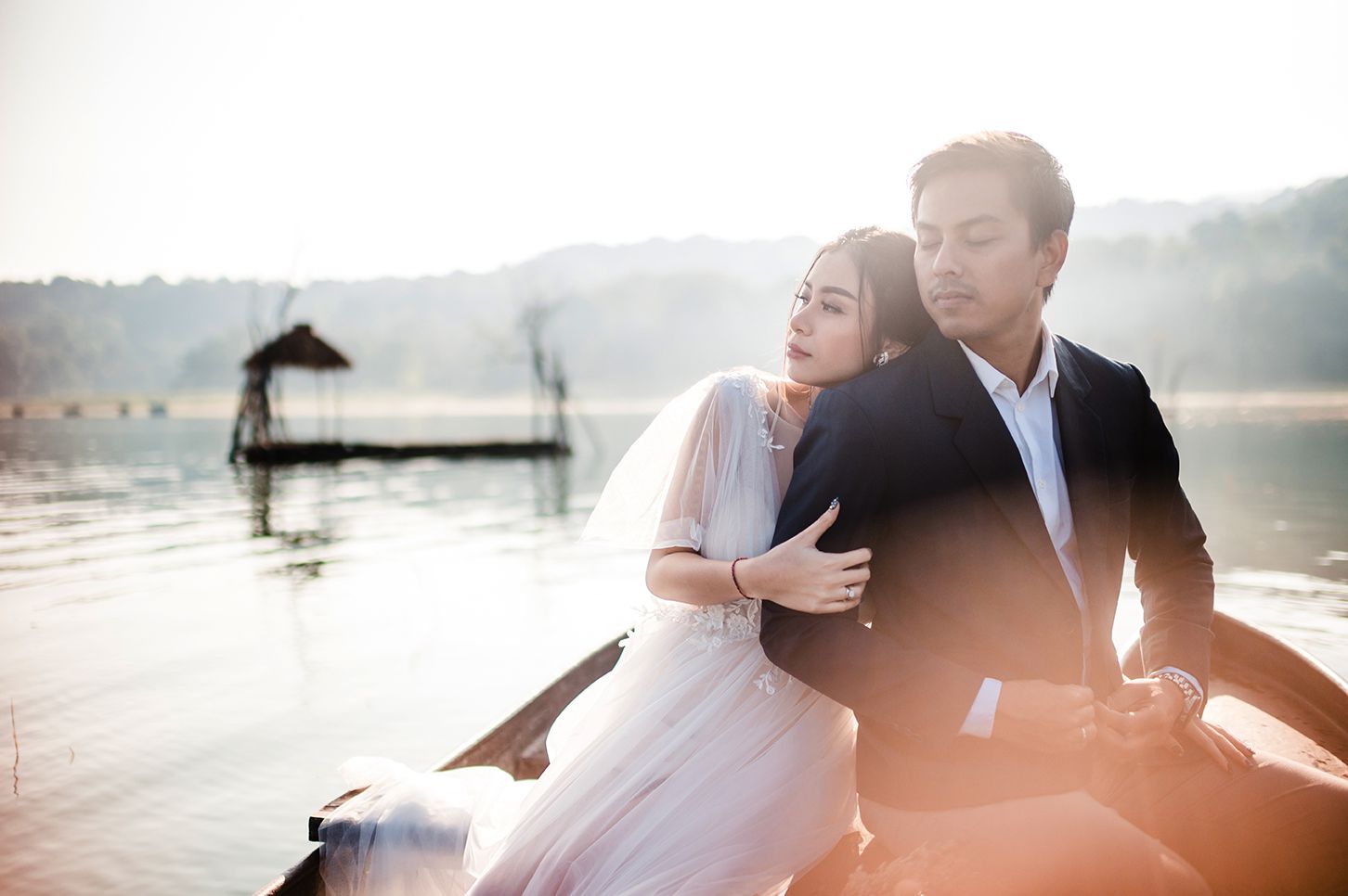 A couple shares a romantic moment on a boat at sunset, with a serene lake and misty mountains in the background.