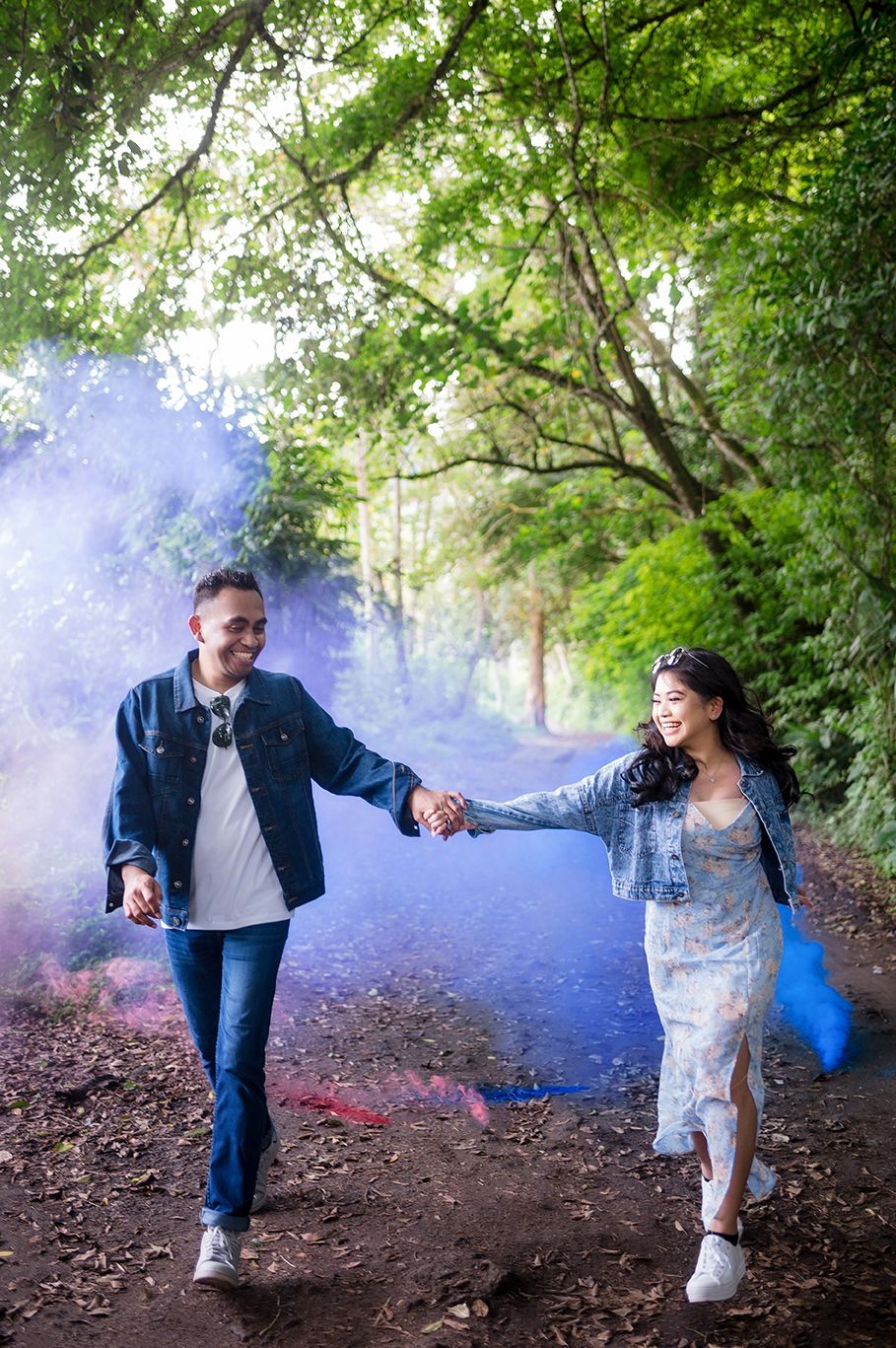 Couple holding hands walking through colorful smoke in forest.