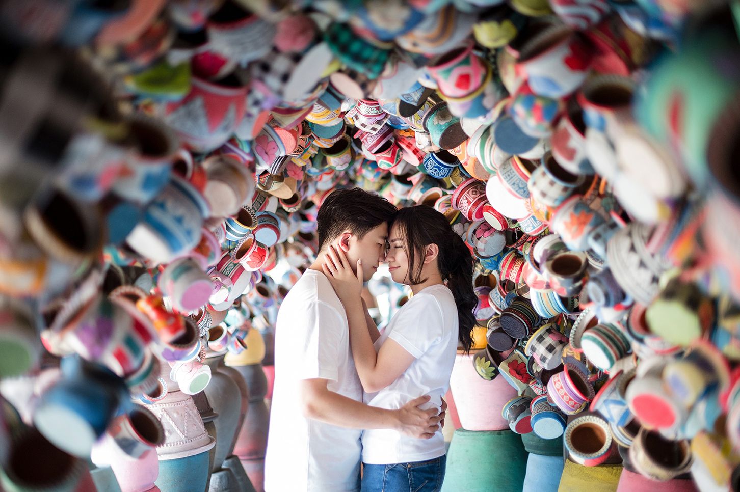Romantic couple kissing surrounded by colorful ceramic pots in a vibrant artistic installation.