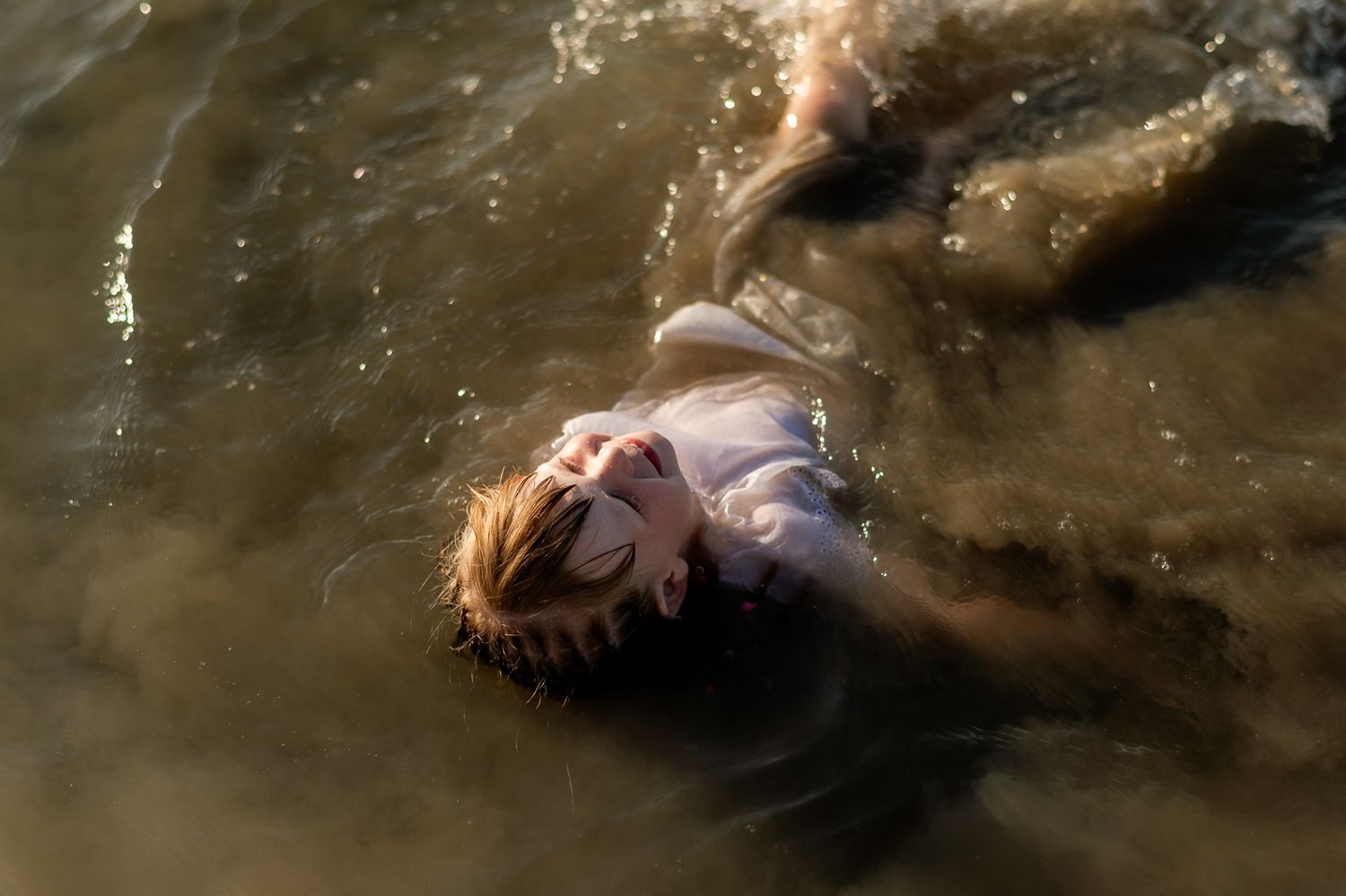Child floats peacefully on back in shallow sunlit water with eyes closed.