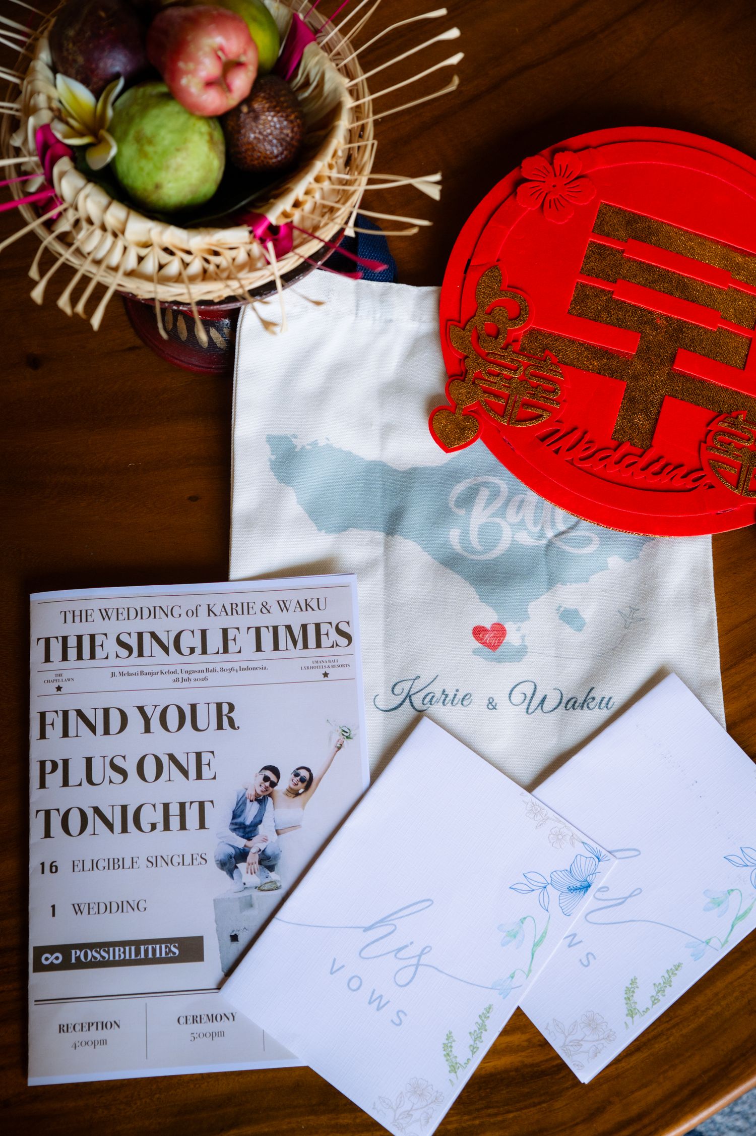 Wedding flat lay with a Single Times newspaper program, Bali map tote bag, red double happiness charm, vow booklets and a fruit offering bas