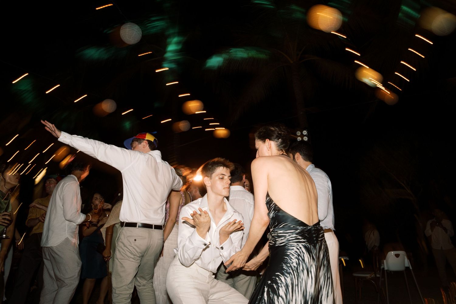 Guests dancing energetically at a wedding reception under twinkling lights at an outdoor evening celebration.