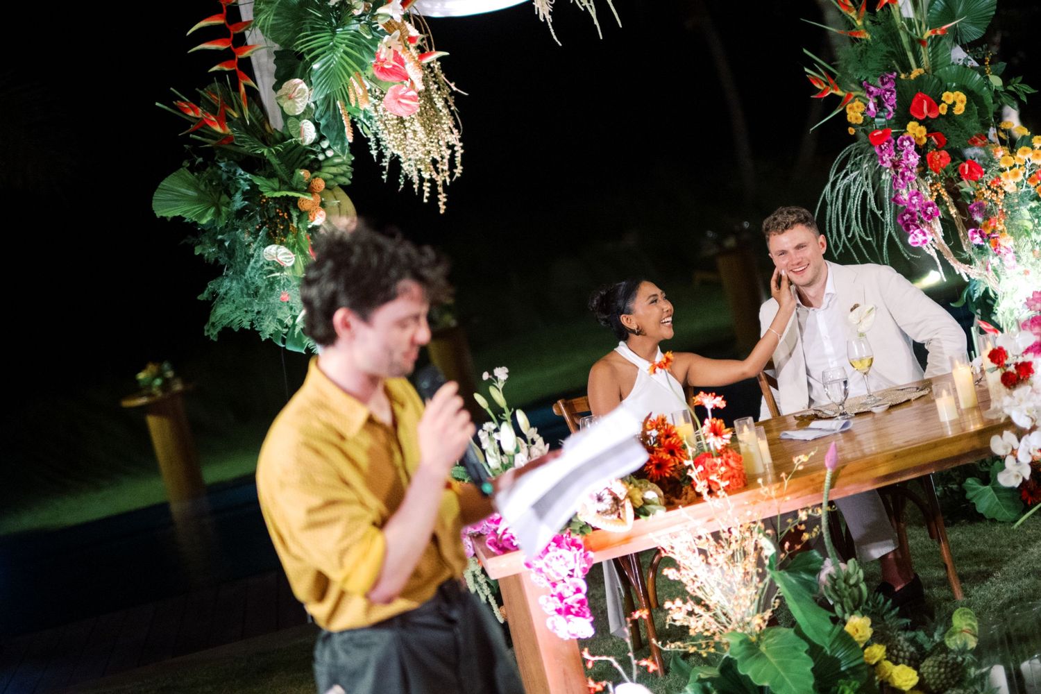 Tropical floral decorated bar with guests socializing at an outdoor evening event.