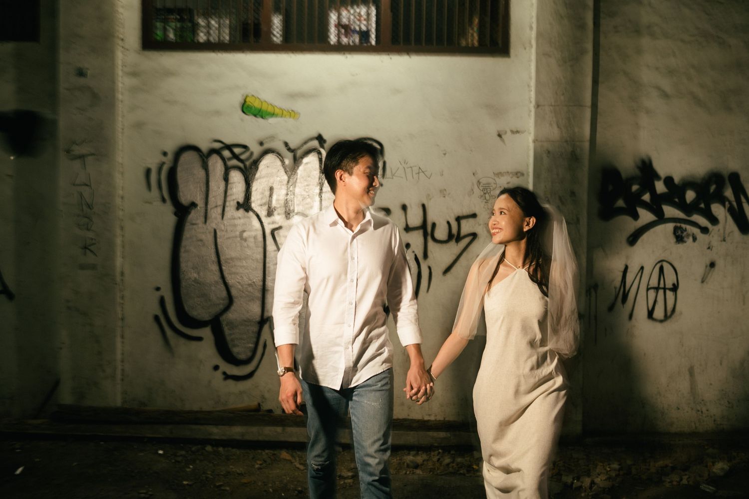Couple holding hands at night in front of graffiti wall, romantic engagement photo session outdoors.