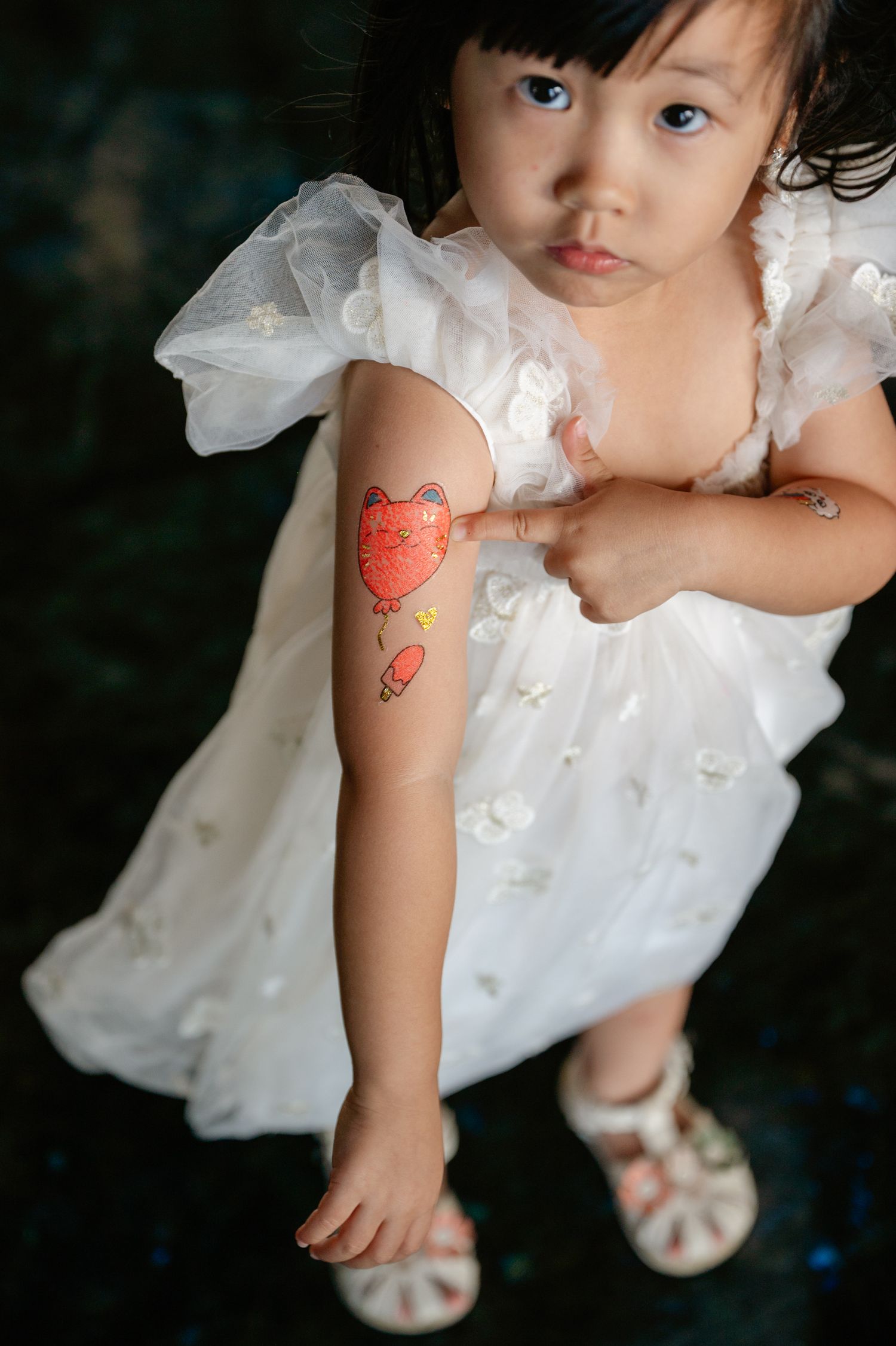 Young girl in white dress showing off a colorful cat temporary tattoo on her arm.