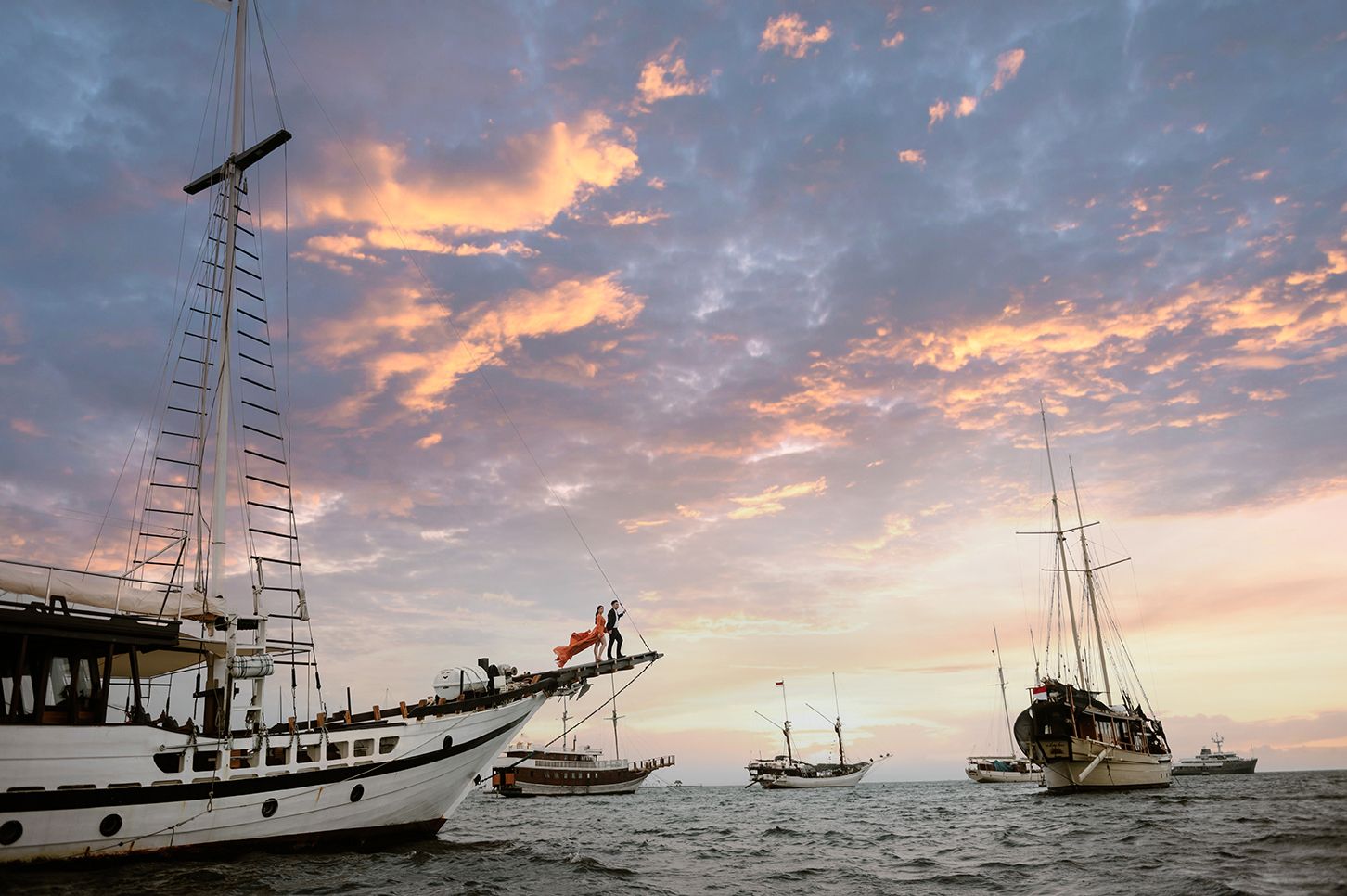 Sailing boats anchored at sea during a vibrant sunset with dramatic clouds.