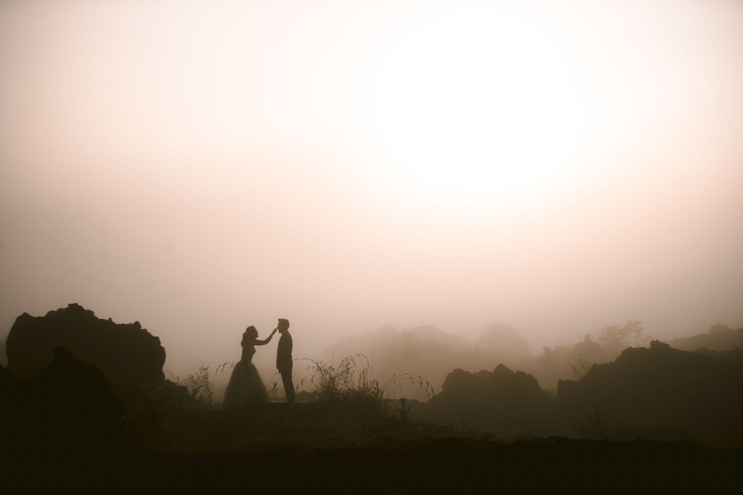 Silhouette of a couple holding hands in a misty, foggy landscape at sunset during a romantic outdoor wedding.