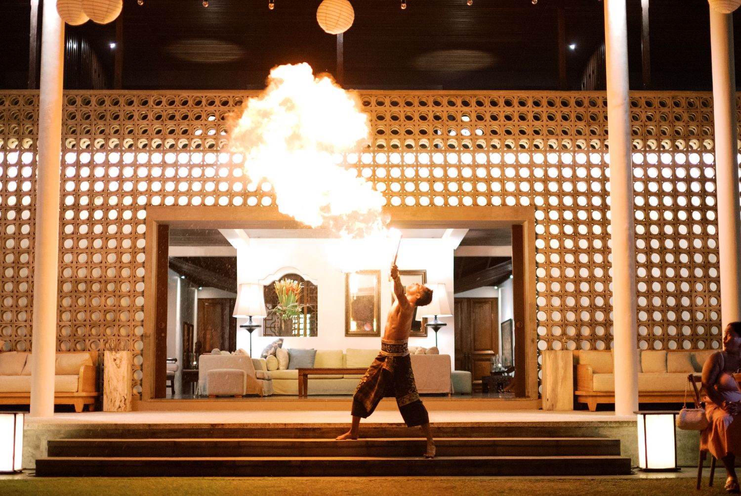 Fire breather performing a dramatic fire show at an outdoor resort venue at night.