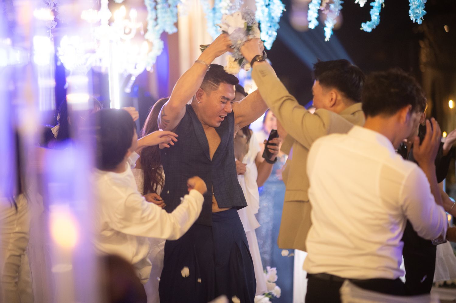 Guests dancing joyfully at an elegant wedding reception with blue floral decorations and festive lighting.