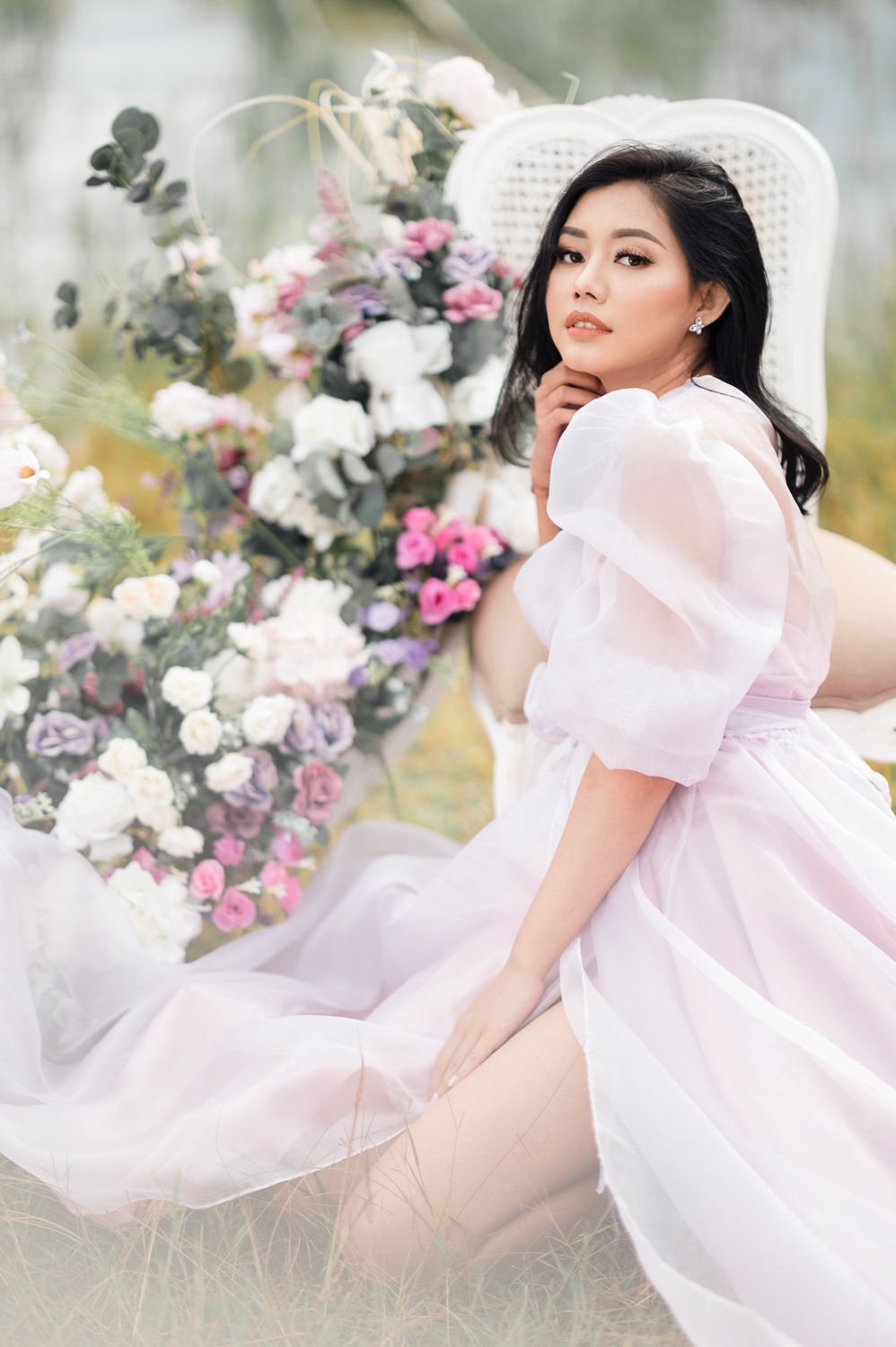 Woman in pink tulle dress and white hat poses gracefully among colorful floral arrangements outdoors.