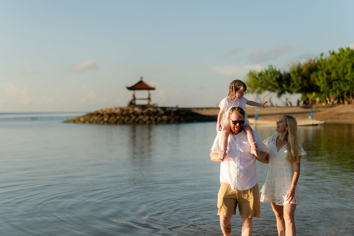 Family of four enjoys a serene beach sunset near a traditional Balinese gazebo.