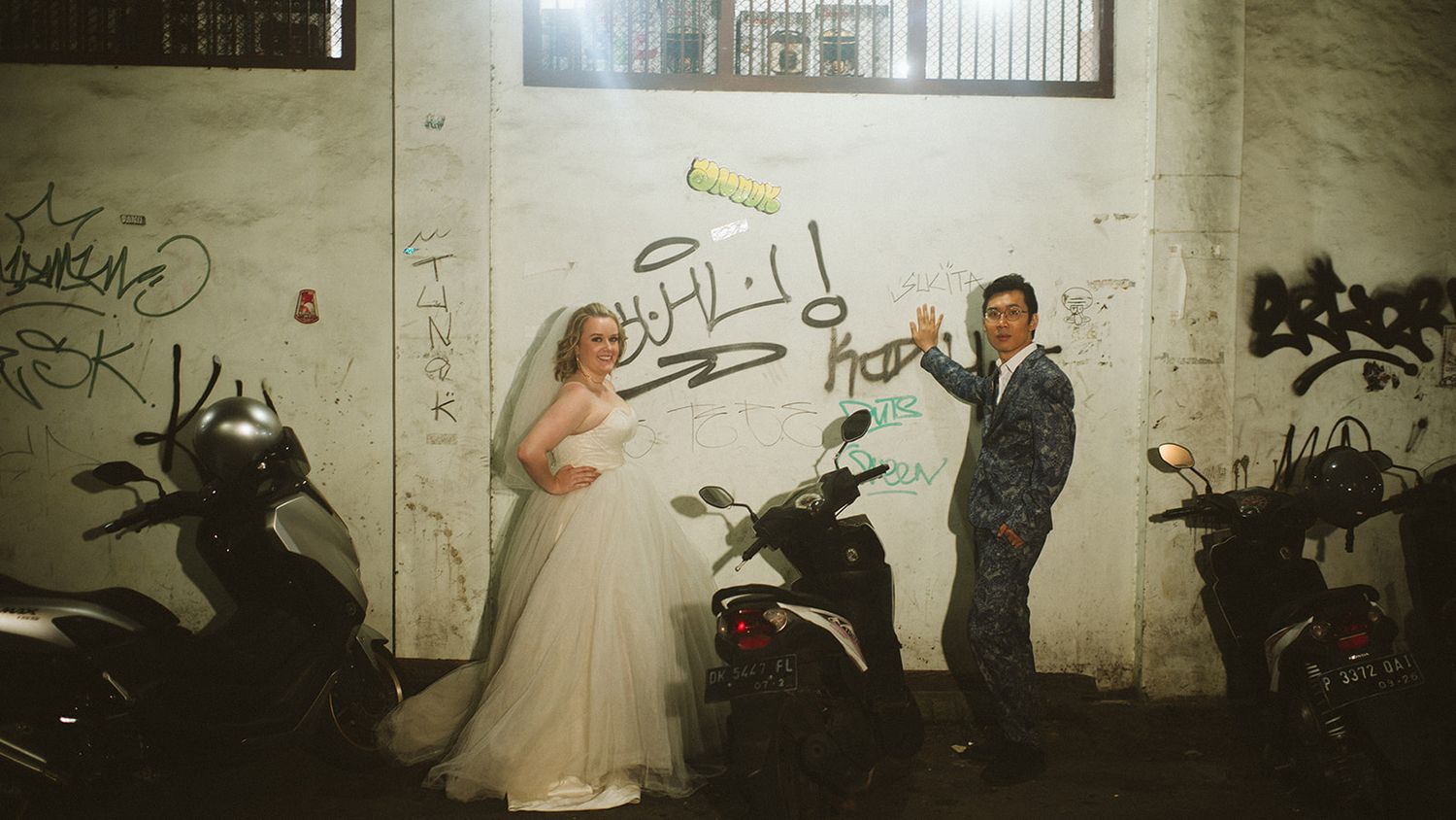 Bride and groom posing in front of a graffiti wall with parked scooters during their wedding photo shoot.