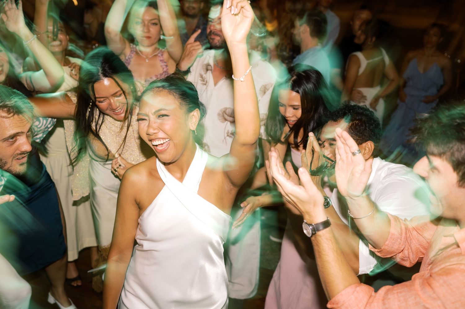 Joyful bride in white dress dancing with guests at lively wedding reception party.
