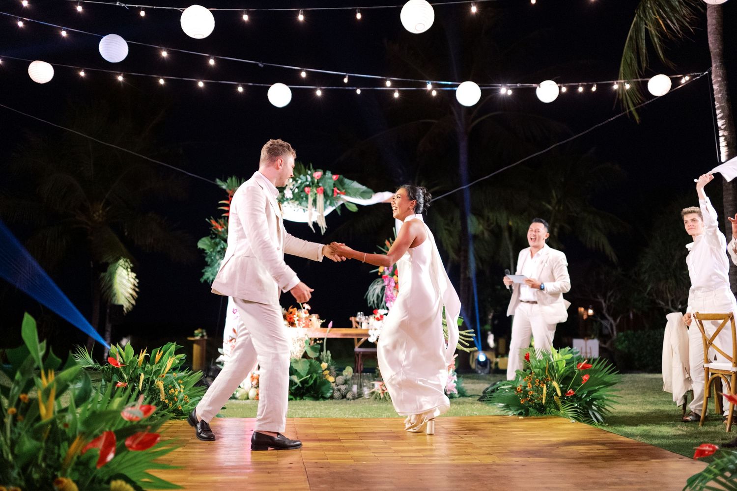 Couple shares first dance at tropical outdoor wedding reception under string lights at night.