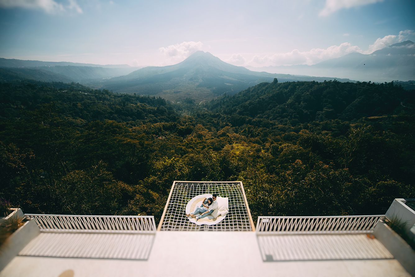 Couple sitting on a white terrace overlooking lush green jungle and volcanic mountain landscape in Bali.