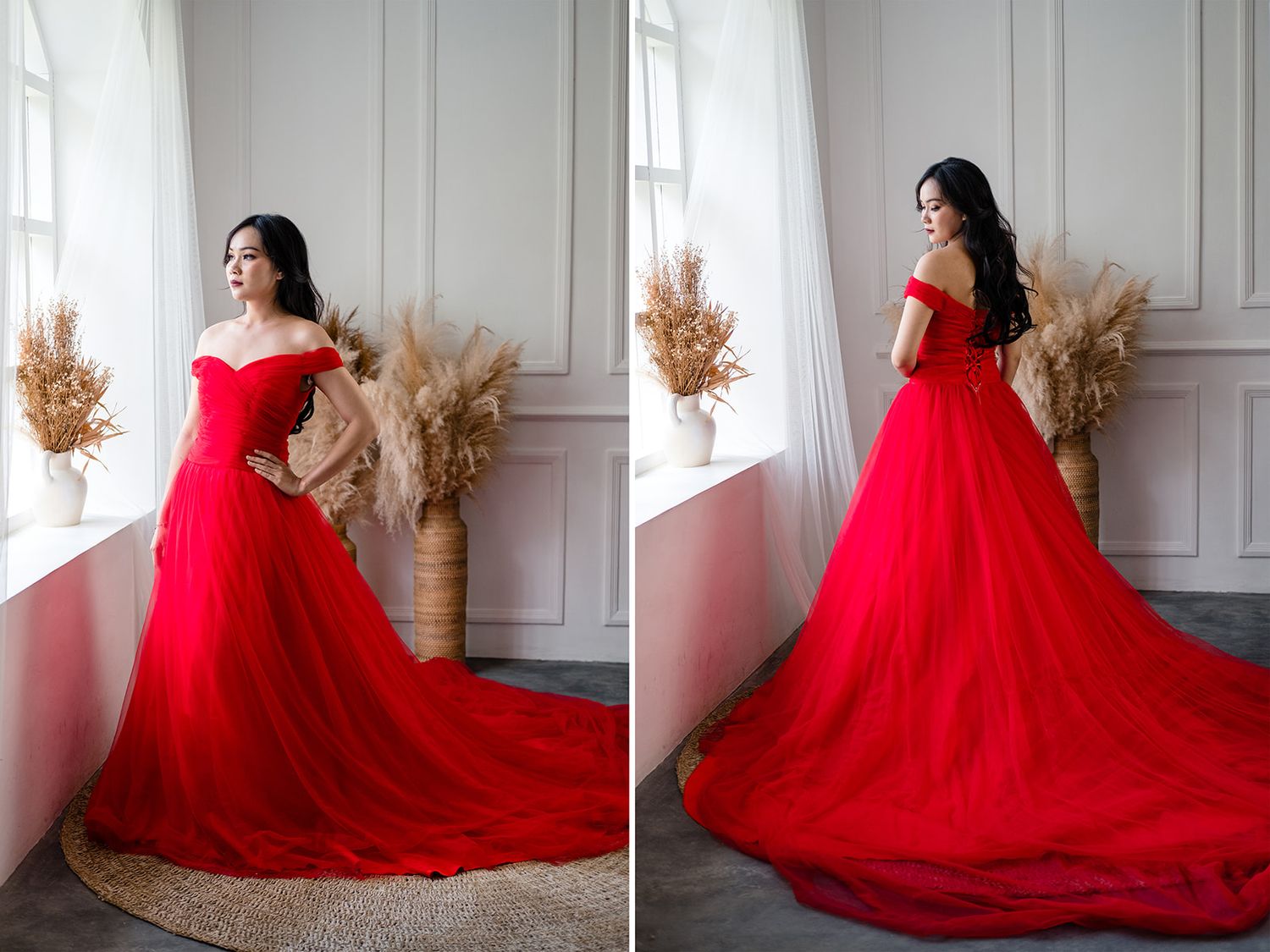 Woman in elegant red off-shoulder tulle ball gown with long train posed by window.
